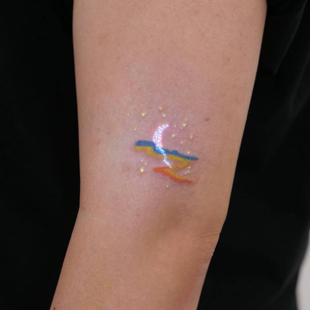 Sea, moon and stars tattoo in uv ink located on the upper arm.