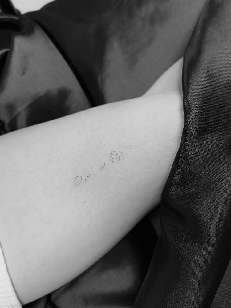 Handwritten lettering and smiley face tattooed on the inner arm.