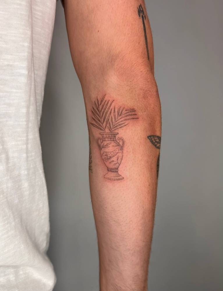 Palm leaves and amphora tattoo located on the inner forearm.