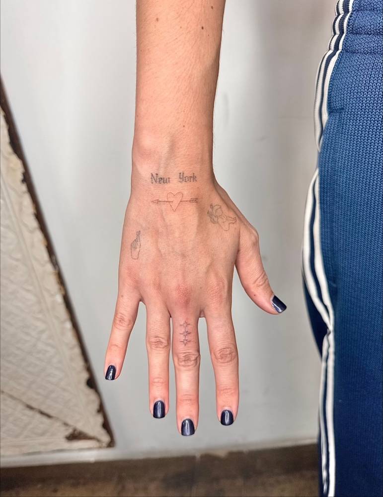 Fine line style heart and arrow tattoo located on the hand.