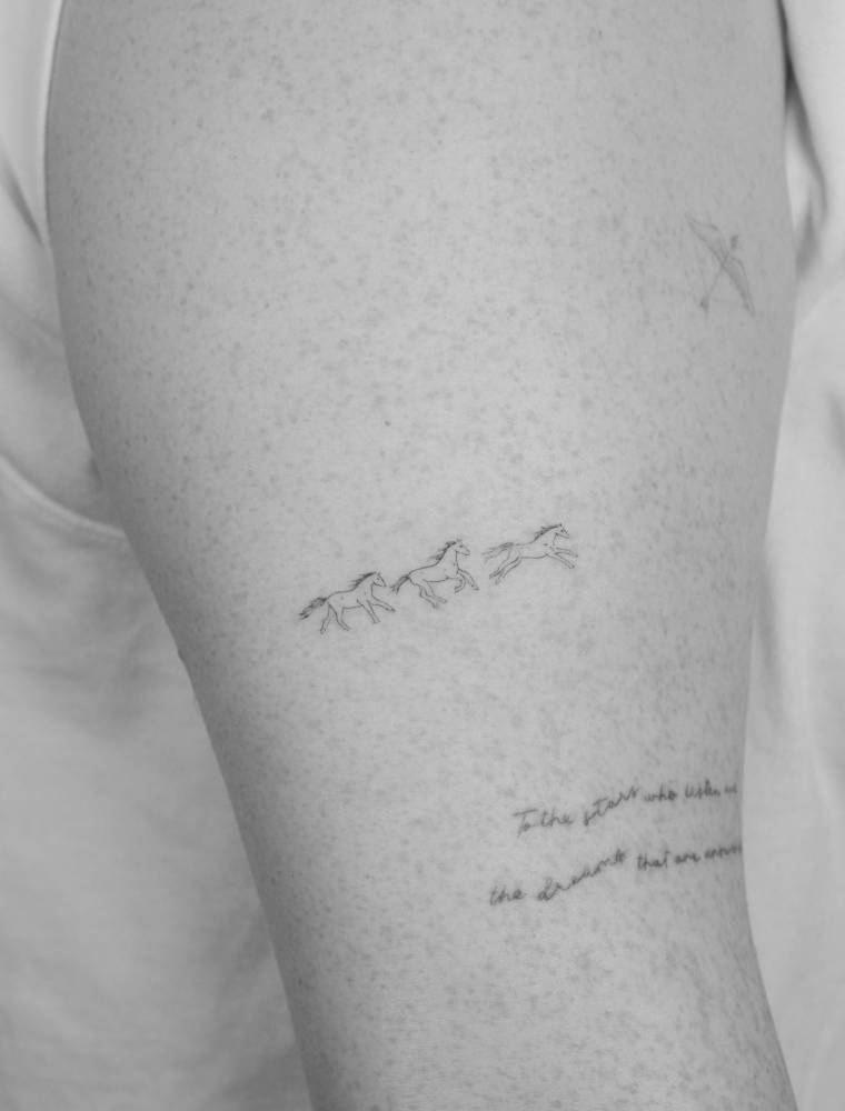 Tiny horses tattooed on the upper arm, done in fine line style.
