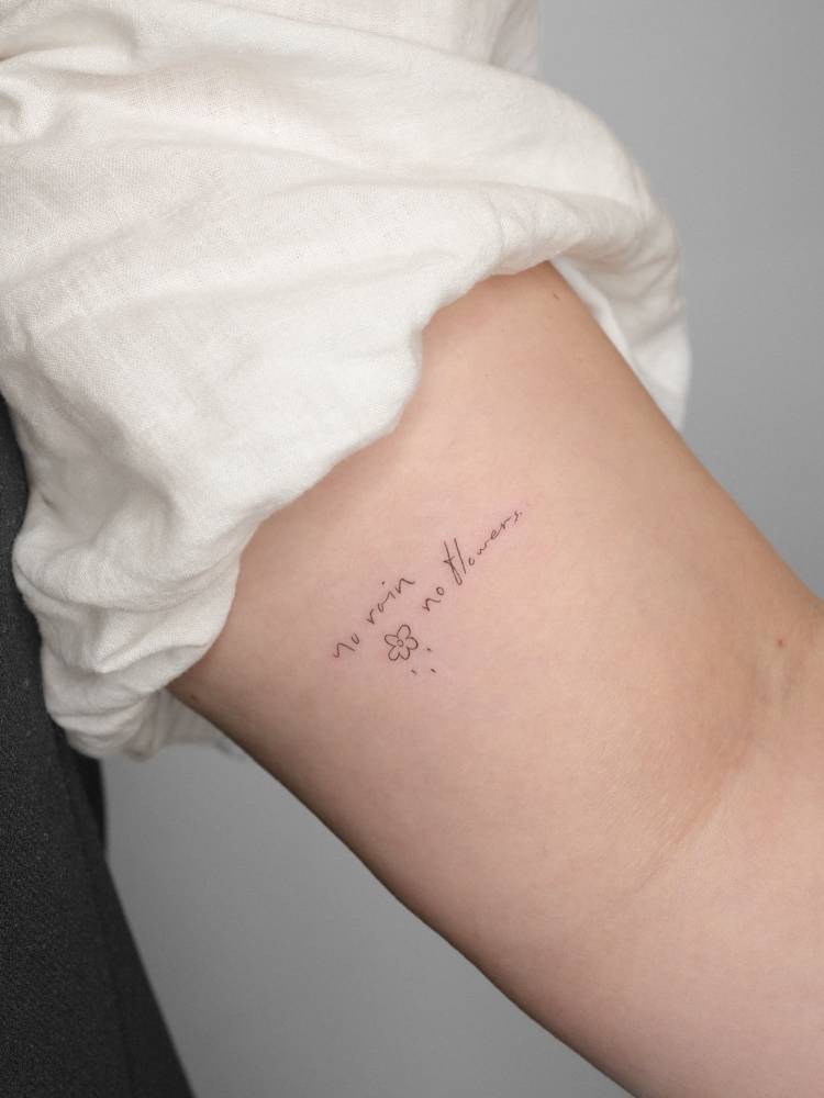 No rain, no flowers tattoo in handwritten font located on the inner arm.