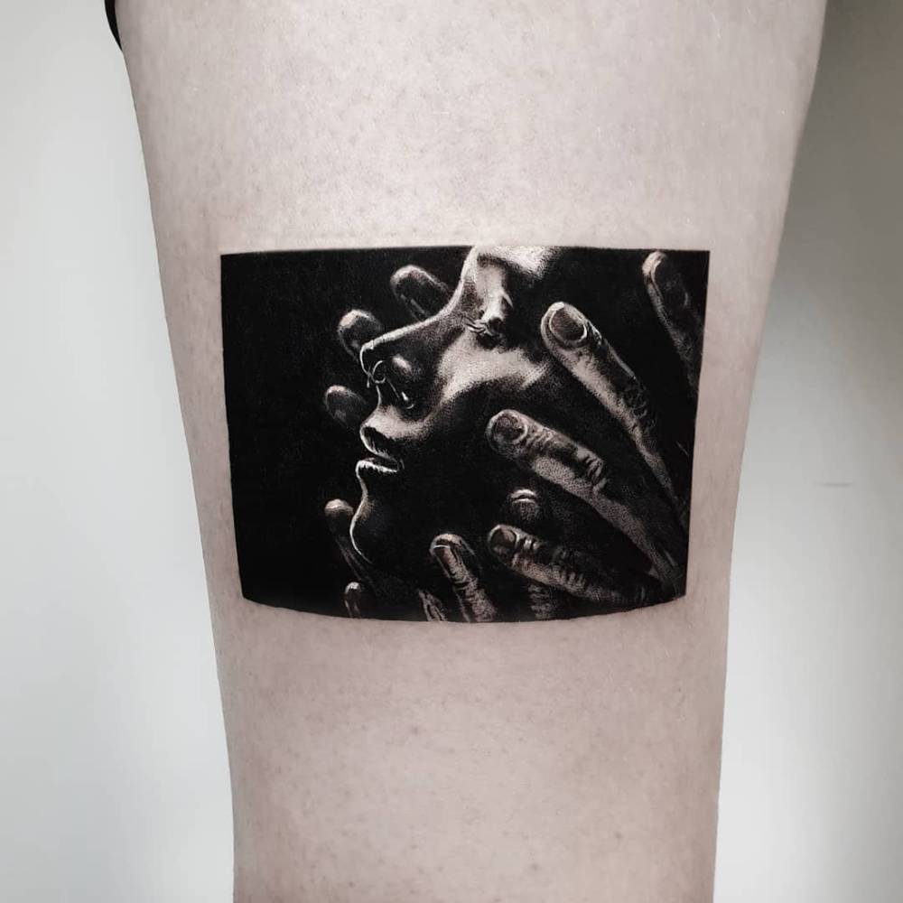 Face and hands tattoo in black and grey style located on the thigh.