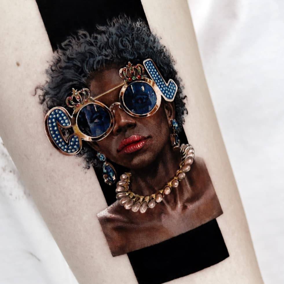 Woman wearing "cool" sunglasses tattooed on the upper arm.