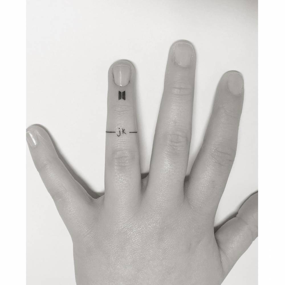 Initials ring tattoo located on the finger, minimalistic style.