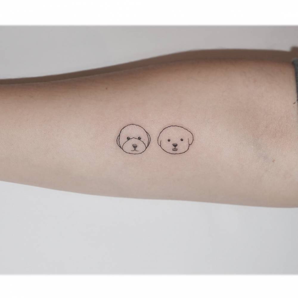 Minimalistic dog portraits tattooed on the inner forearm.