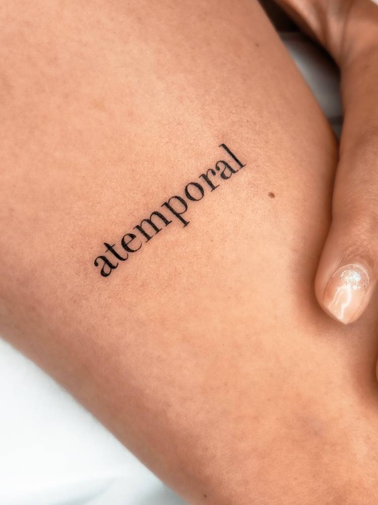Lettering tattoo of the word “atemporal” in serif font.
