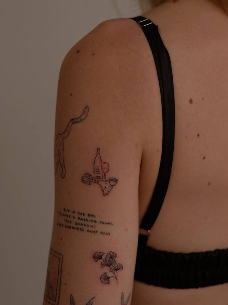Wine and ginkgo leaves tattoos located on the upper arm, fine line style.