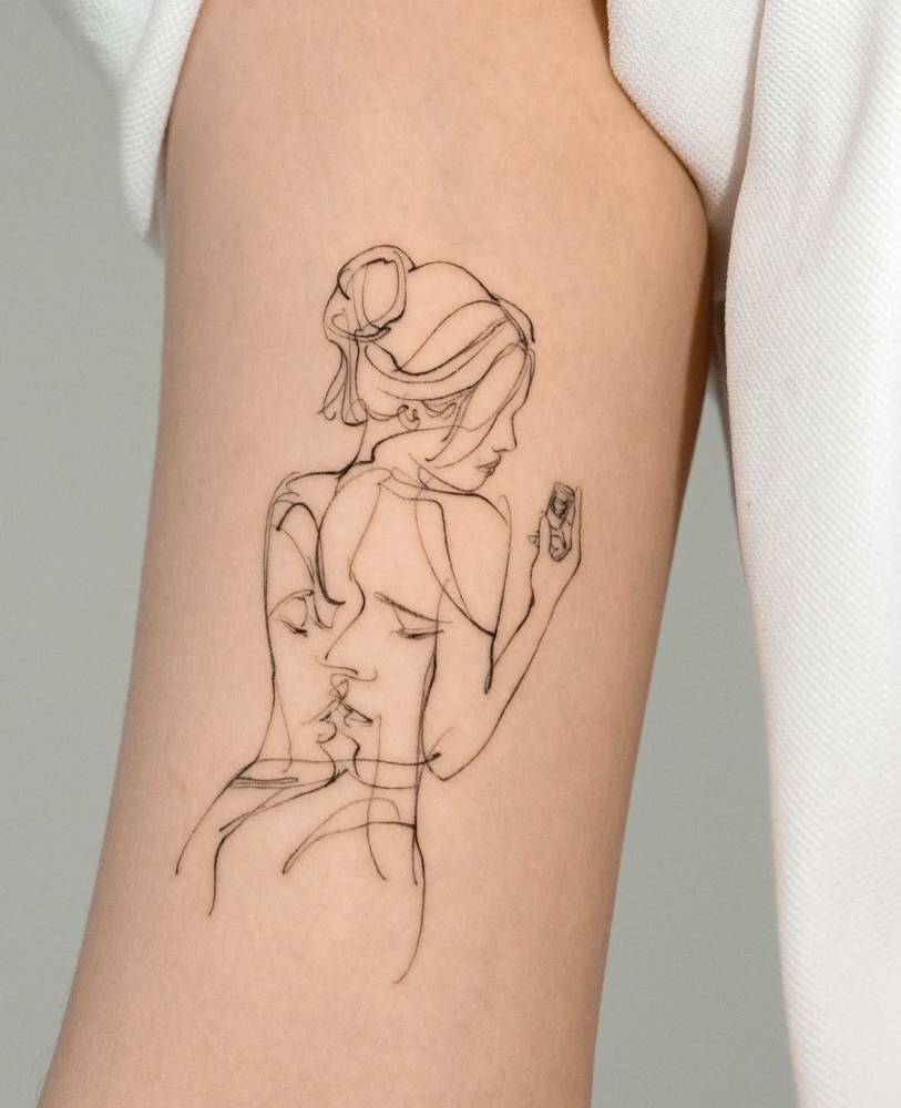 Sketch work style woman and kiss tattoo located on the bicep.