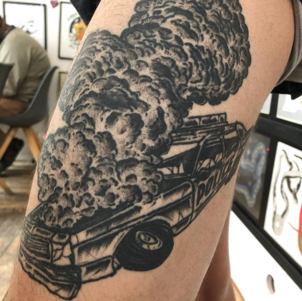 Police car burning tattooed on the thigh, blackwork style.