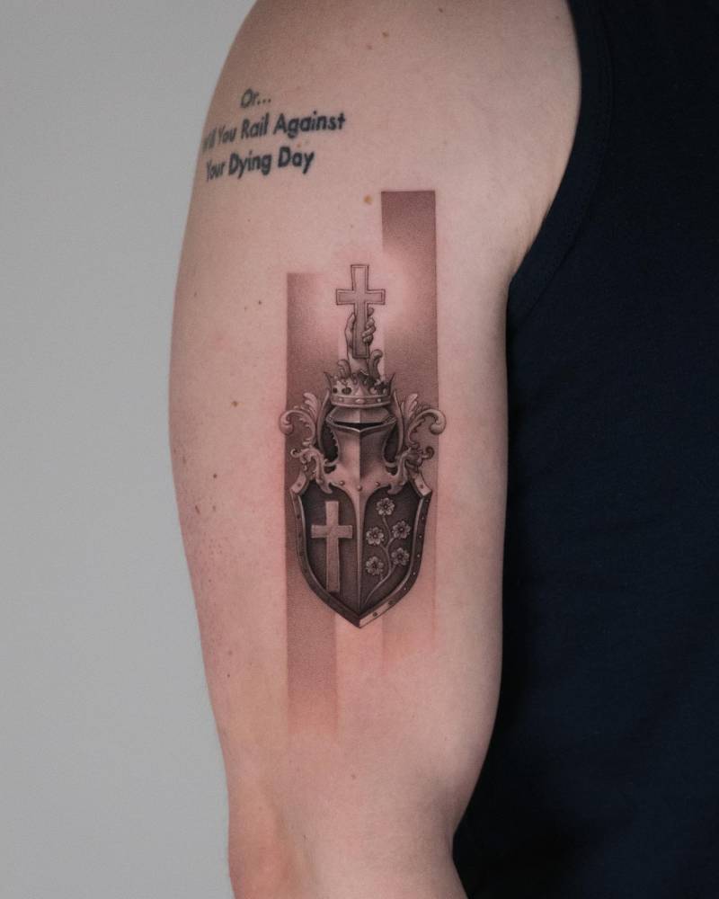 Shield, helmet and cross tattoo located on the upper arm, micro-realistic style.