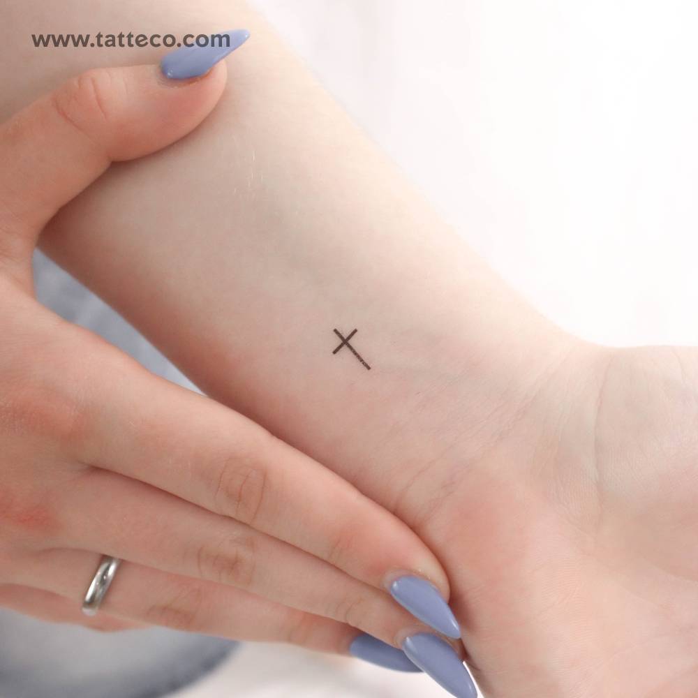 Small minimalist cross temporary tattoo located on the wrist.