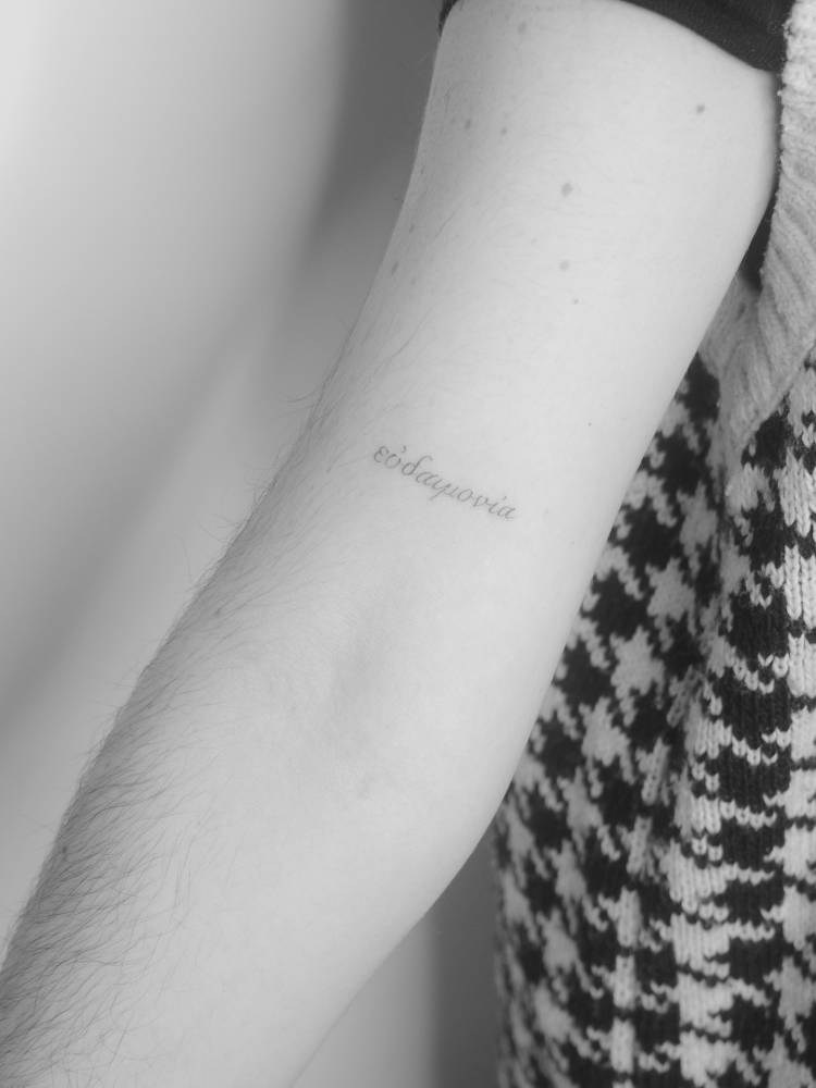 "Eudaimonia" in greek lettering tattooed on the bicep.