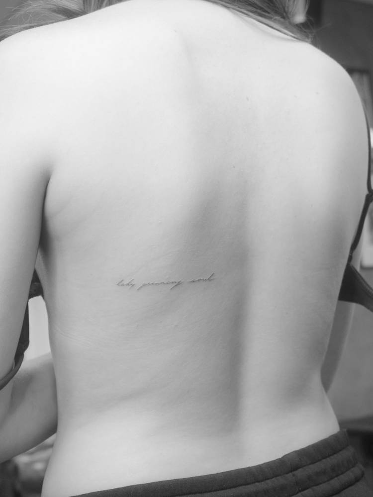 "Lady grinning soul" lettering tattoo located on the back.