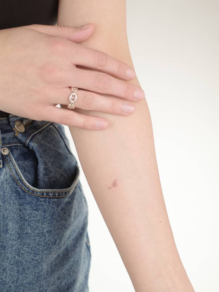 Tiny tattoo of the letter "M" placed on the inner forearm.