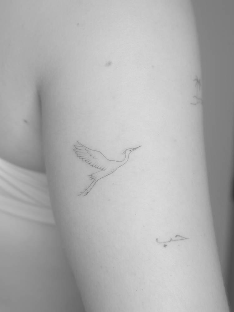 Egret tattoo in fine line style placed on the upper arm.
