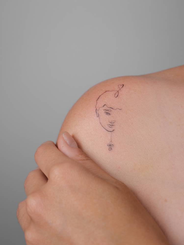 Fine line style face tattoo located on the shoulder.