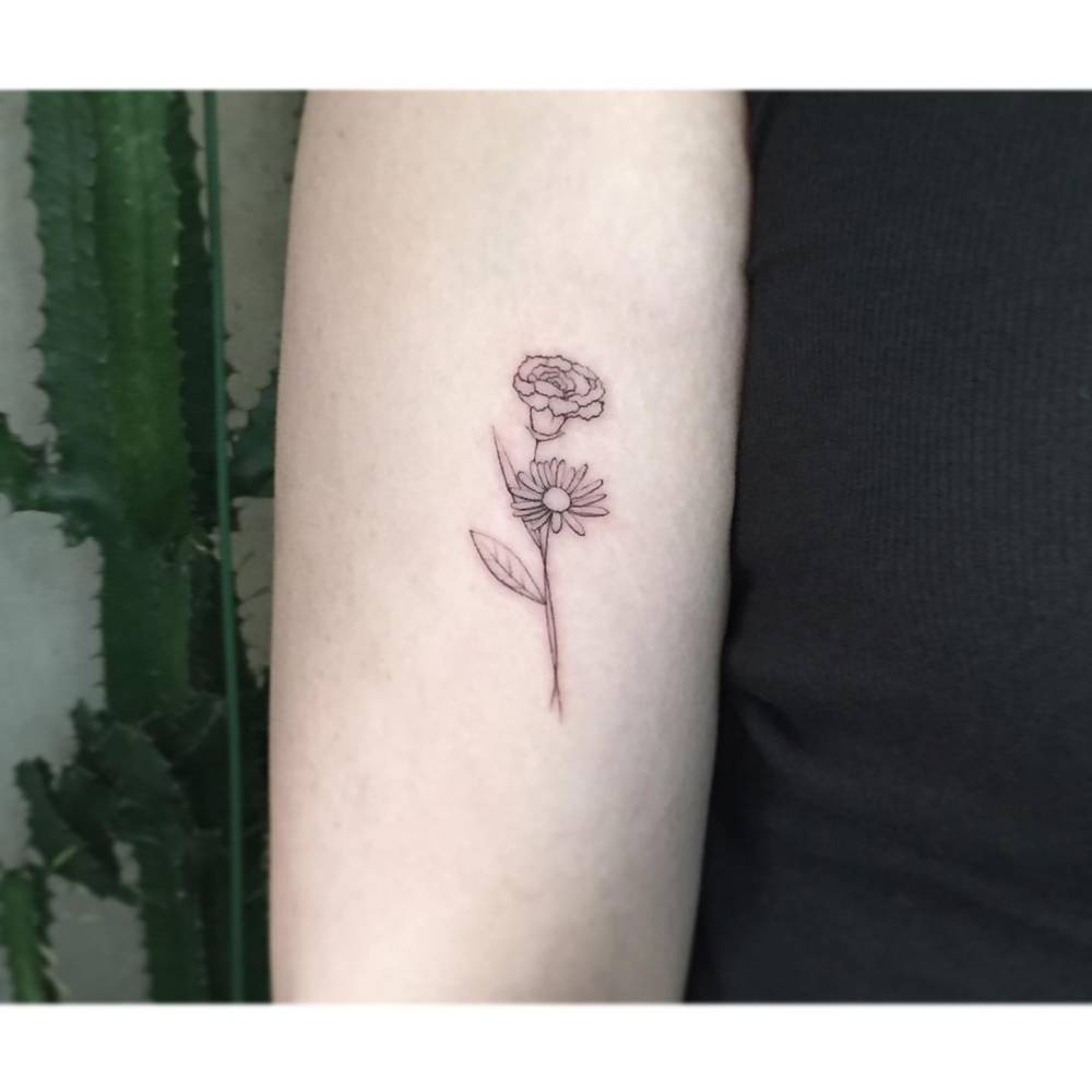 Carnation and daisy flower tattoo located on the upper arm, fine line style.