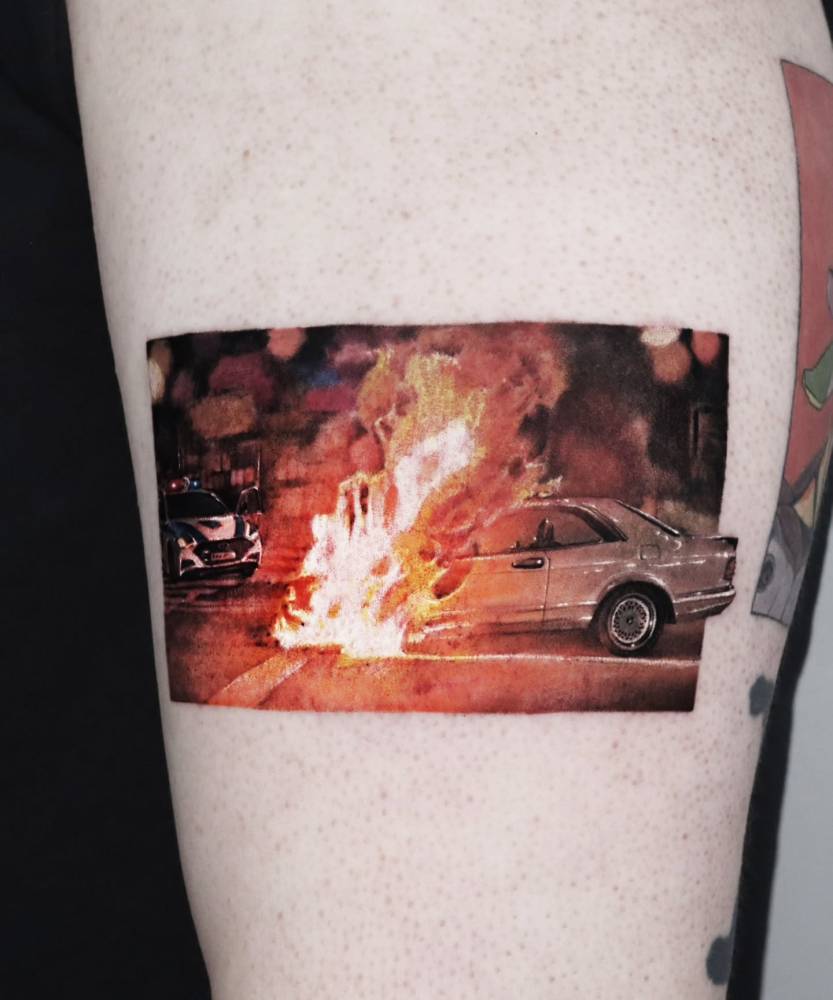 Burning car tattoo in micro-realistic style placed on the upper arm.