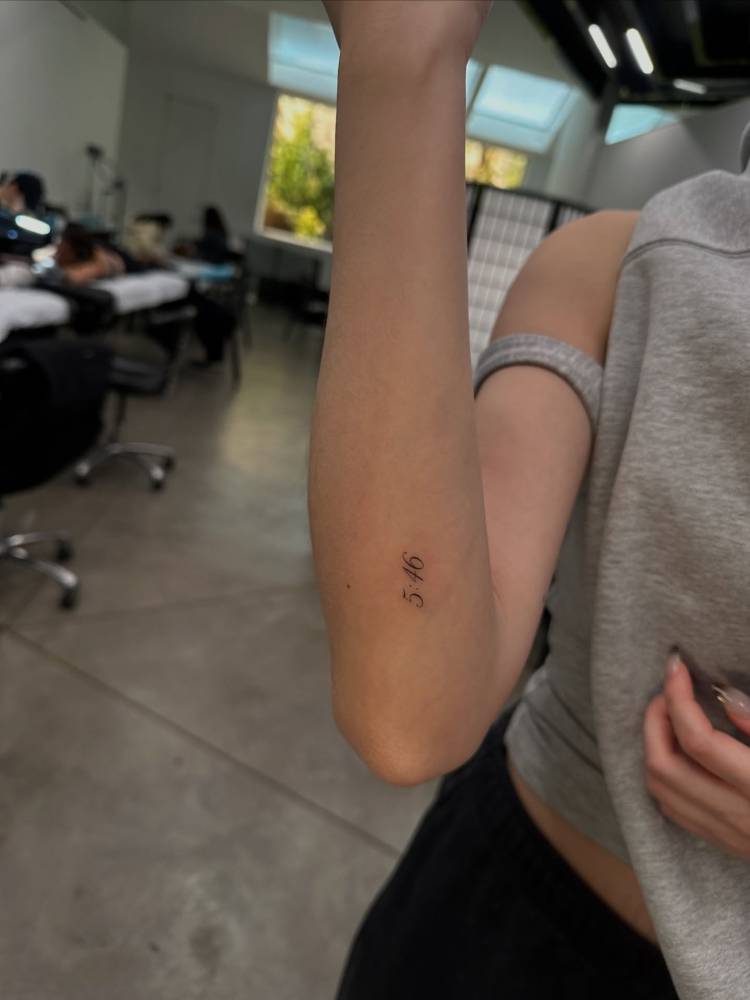Hour tattoo in serif font located on the forearm.