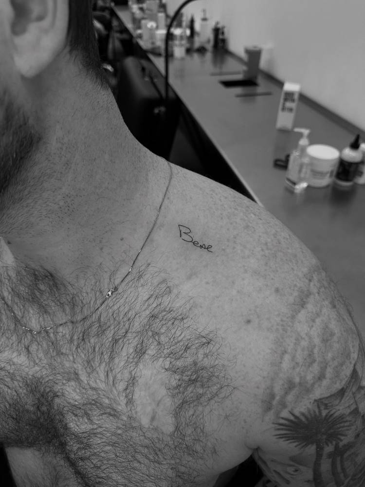 Handwritten font word "bear" tattooed on the top of shoulder.