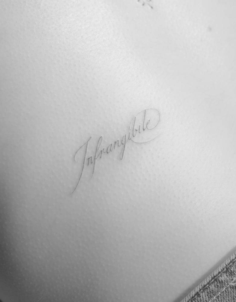 "Infrangible" lettering tattoo in script font located on the lower back.