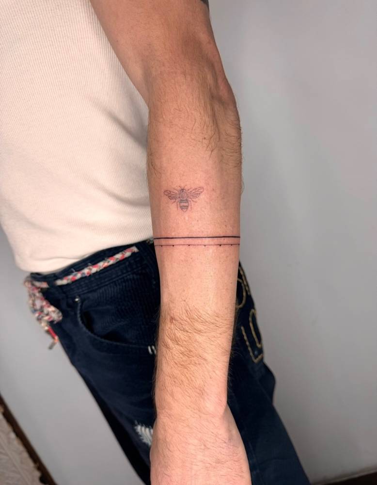 Bee and armband tattoos located on the forearm.