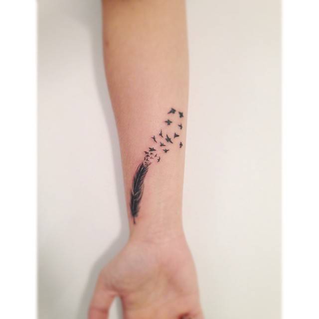 Feather and flying birds tattoo located on the wrist, illustrative style.