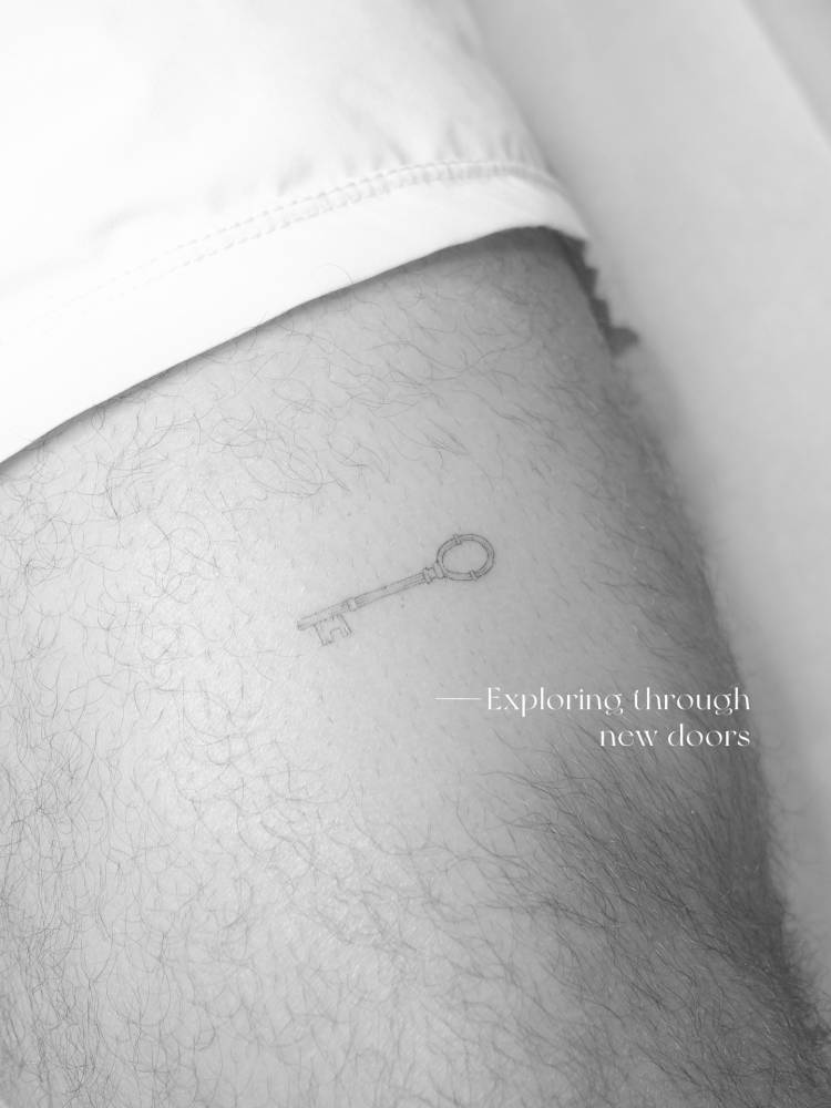 Fine line style little key tattoo located on the upper arm.