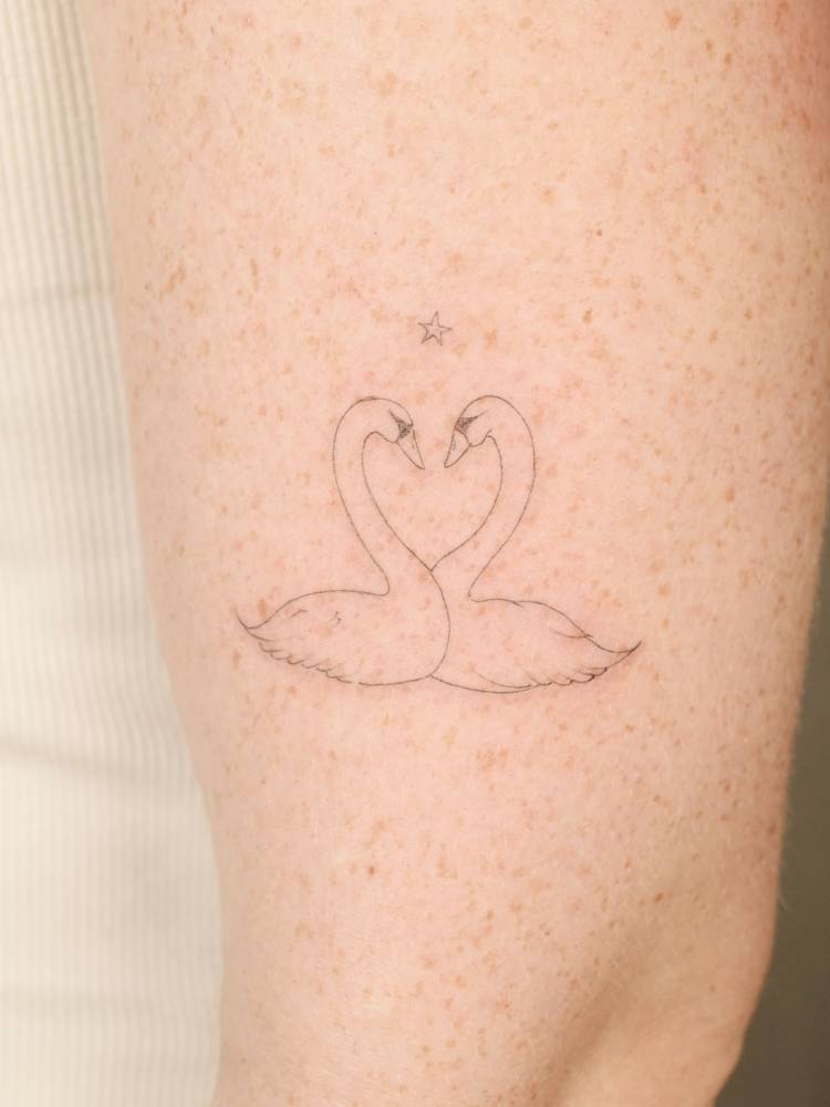 Swan couple tattoo located on the upper arm, fine line style.