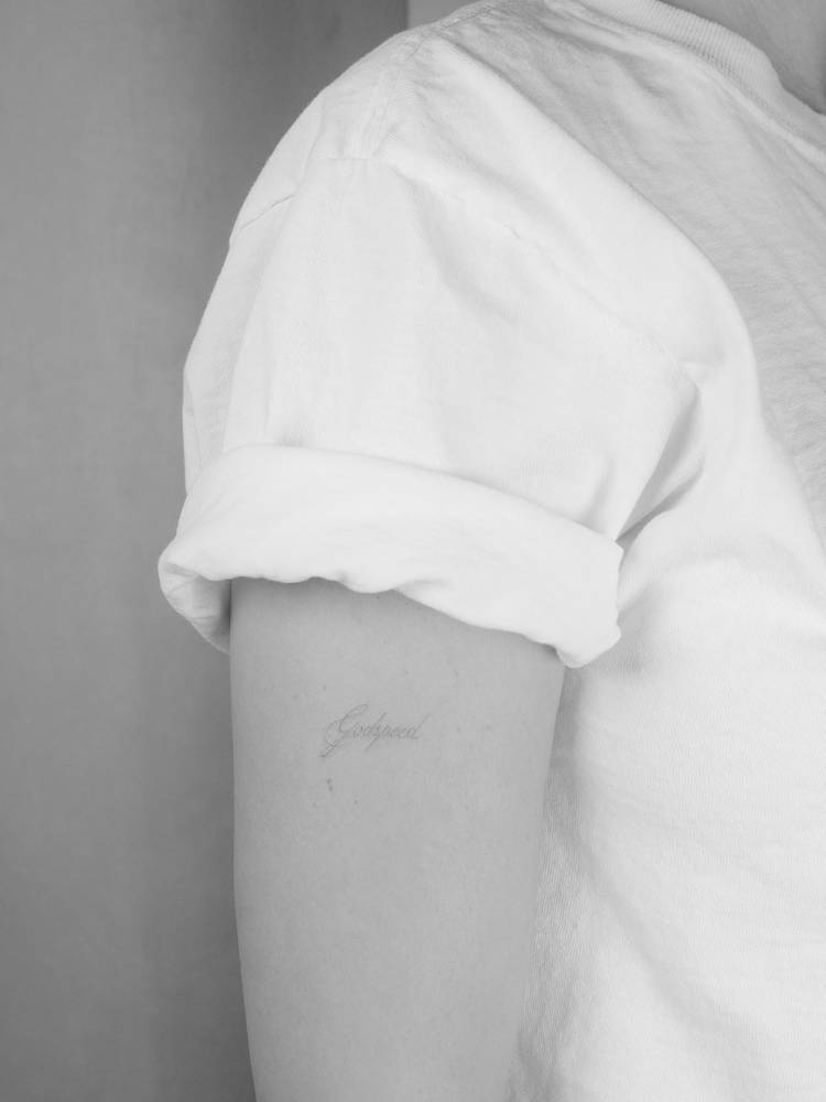 Lettering tattoo of the word "Godspeed" located on the upper arm.