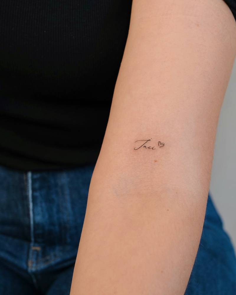 Name "Jaci" and minimalistic heart tattoo located on the bicep.
