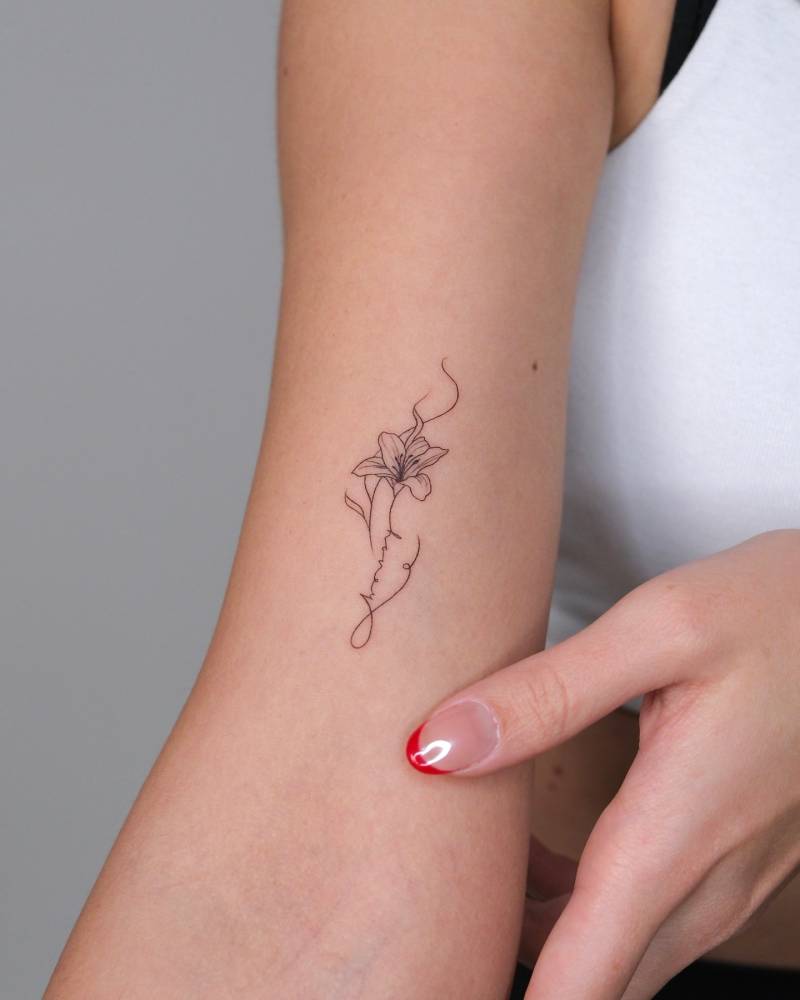 Fine line style word "honey" and lily flower tattoo placed on the bicep.
