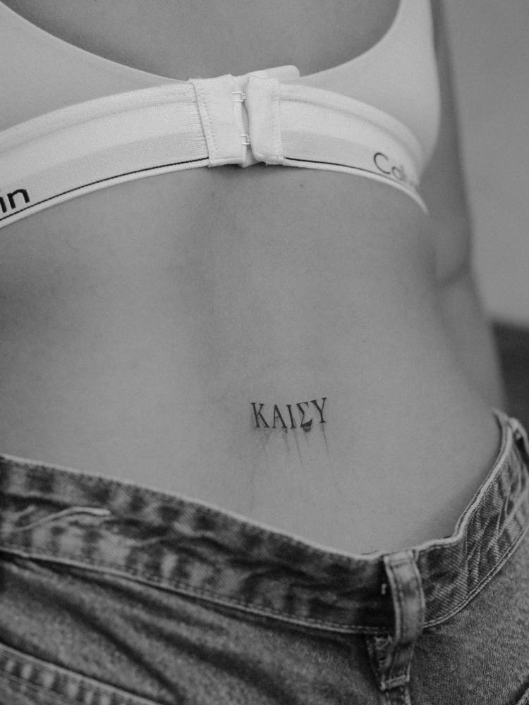 Greek lettering tattoo located on the lower back.