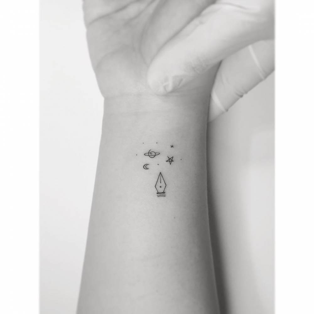 Pen tip and universe tattoo in minimalistic style located o the wrist.