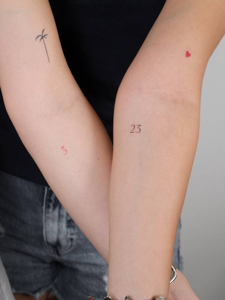 Tiny lettering tattoo of the number "23" located on the inner forearm.