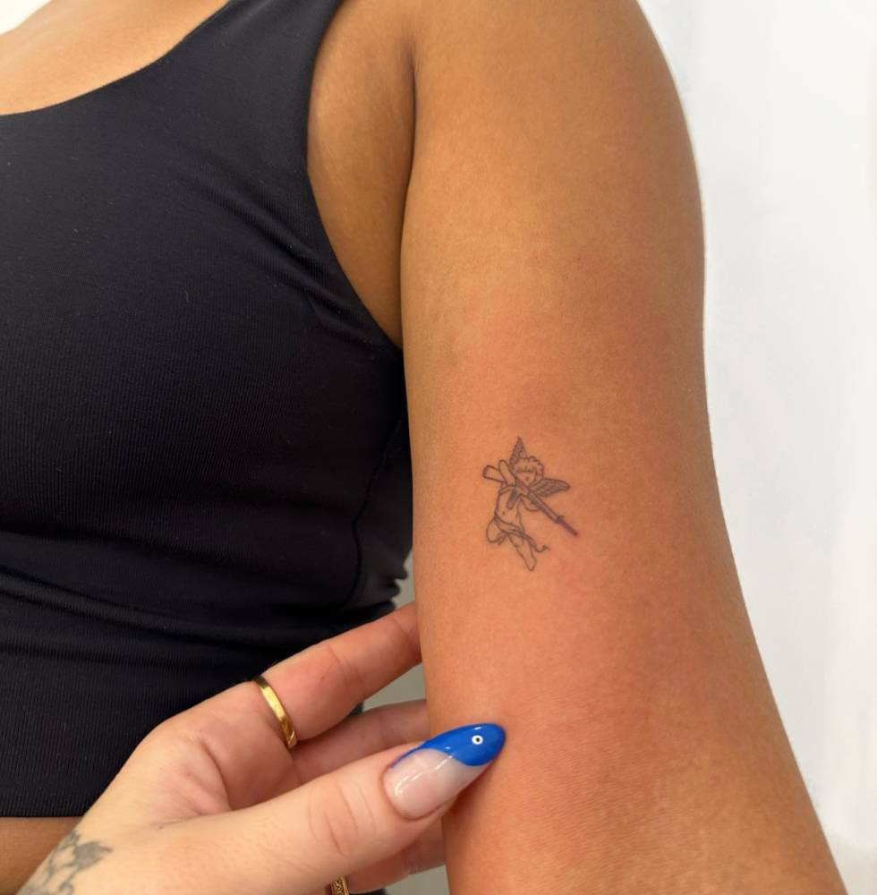 Fine line style armed cherub tattoo located on the bicep.
