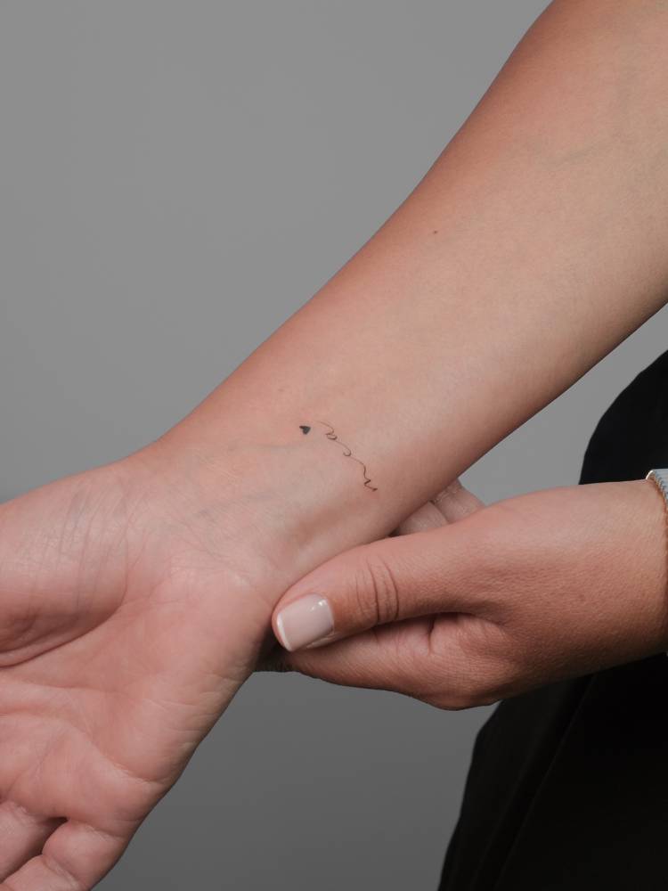 Initials and minimalistic heart tattoo located on the wrist.