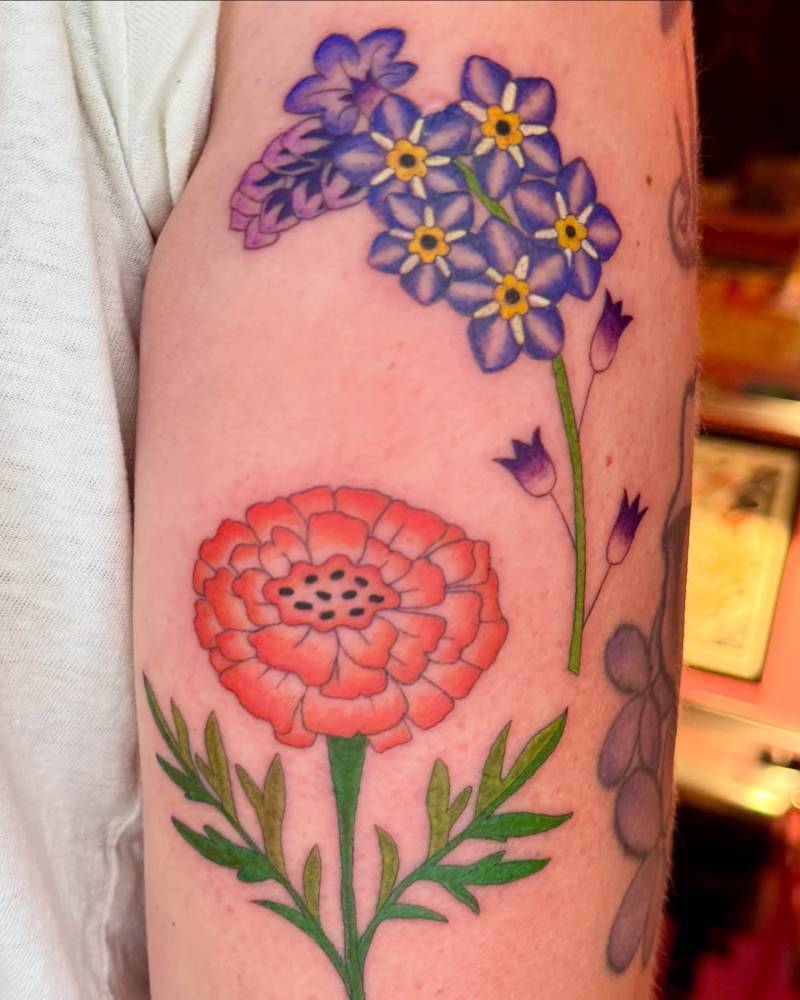 Marigold and forget-me-not flowers tattooed on the tricep, illustrative style.