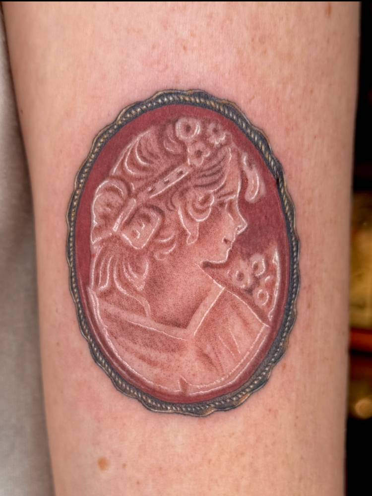 Brooch tattoo in illustrative style placed on the upper arm.