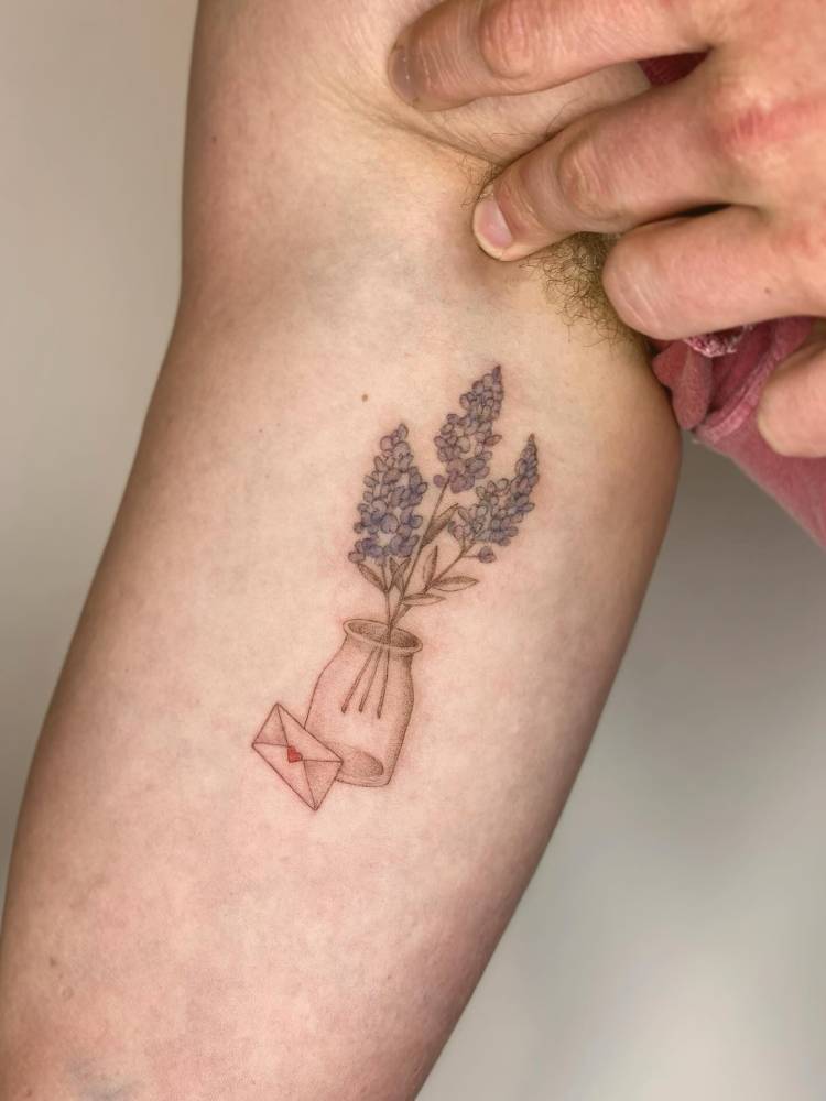 Flowers in a bottle and love letter tattoo located on the inner arm.