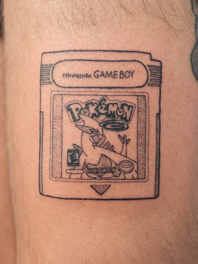 Game Boy cartridge tattoo located on the thigh, illustrative style.