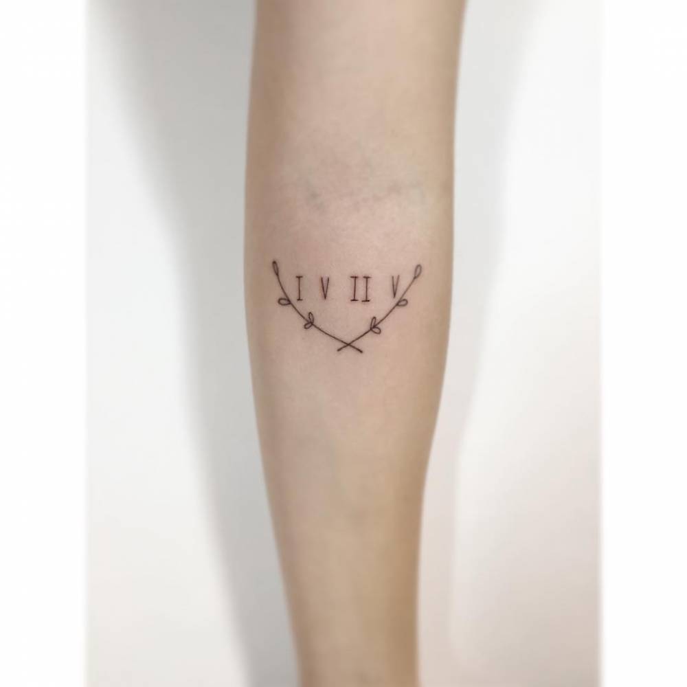 Laurel wreath and roman numerals tattooed on the inner forearm.