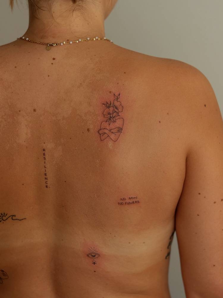 Flower head self hug tattoo located on the shoulder blade.