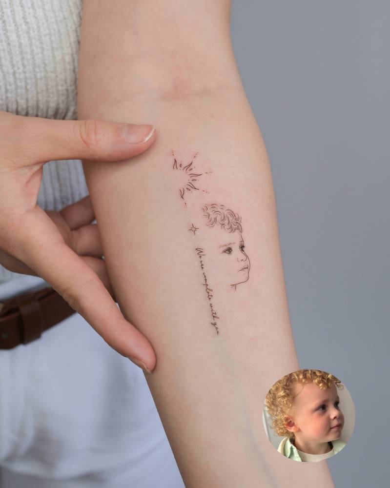 Child portrait and word "we are complete with you" tattooed on the inner forearm.