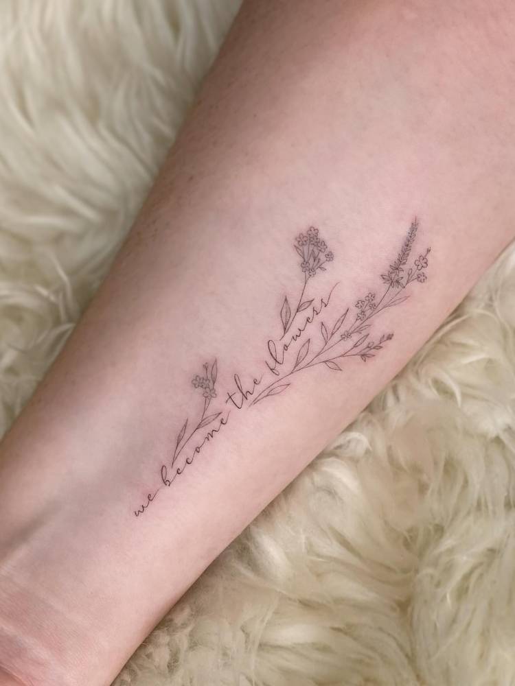 "We become the flowers" lettering tattoo located on the wrist.