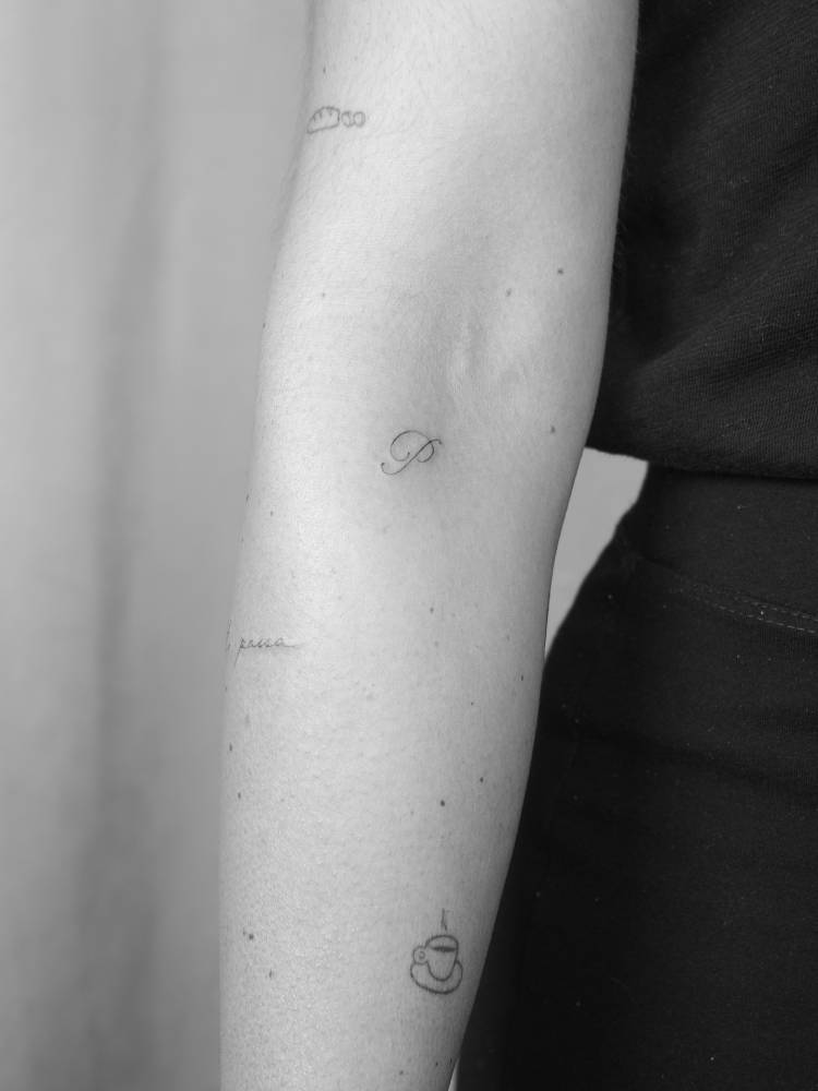 Script font letter "P" tattoo located on the inner forearm.
