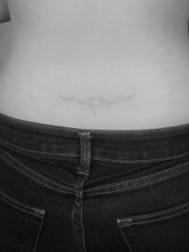 Tribal heart tattoo located on the lower back, fine line style.
