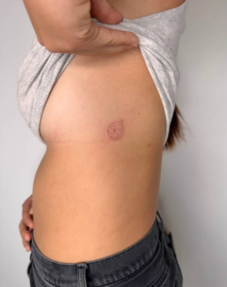 Fine line style small fig tattoo placed on the side boob.