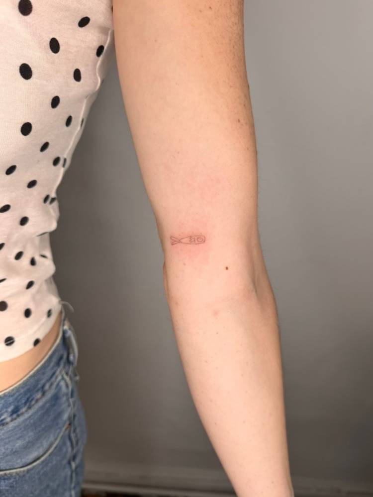 Minimalist fish tattoo in fine line style placed on the inner arm.